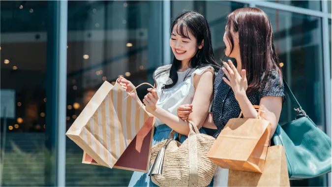 福岡市早良区の土地について徹底解説、買い物袋をたくさんぶら下げ、歩きながら友人と談笑する二人組の女性